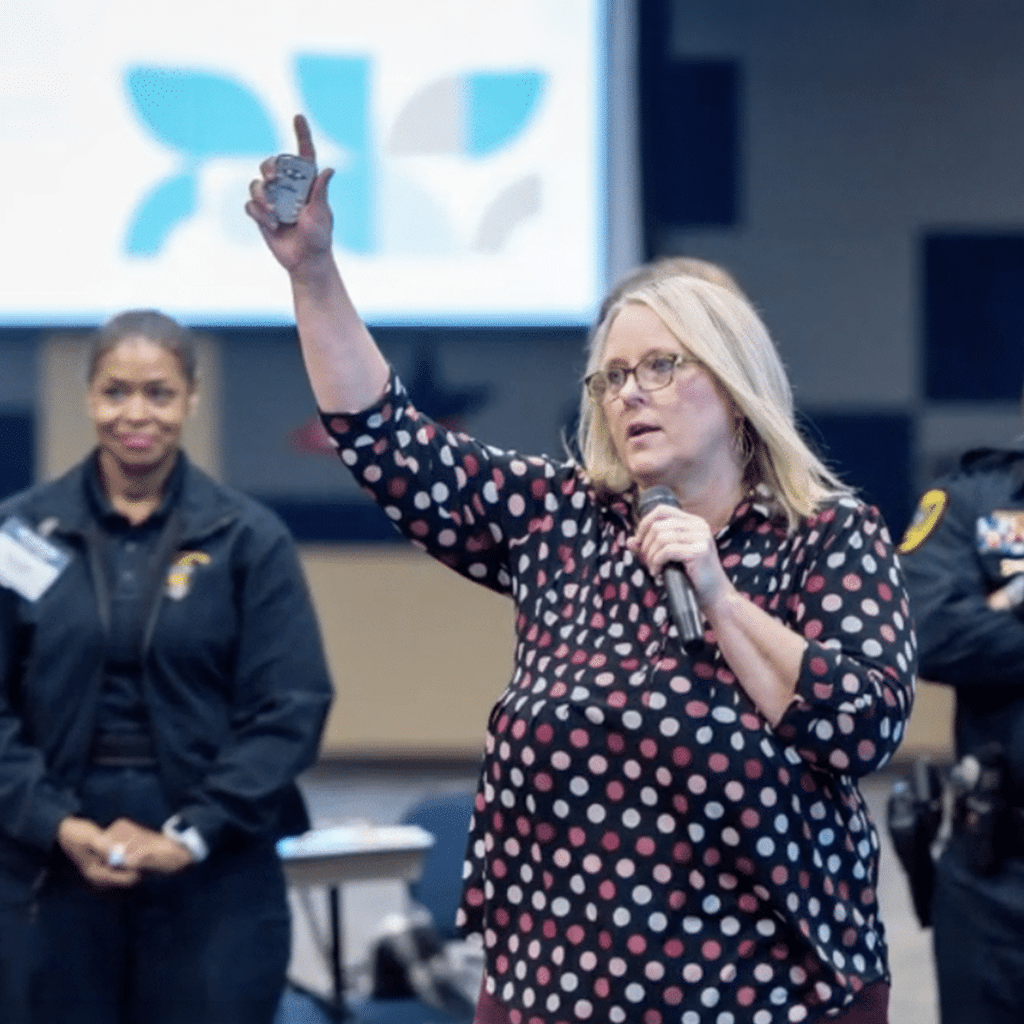 Woman holding a microphone with her other hand up in the air, presenting to a group
